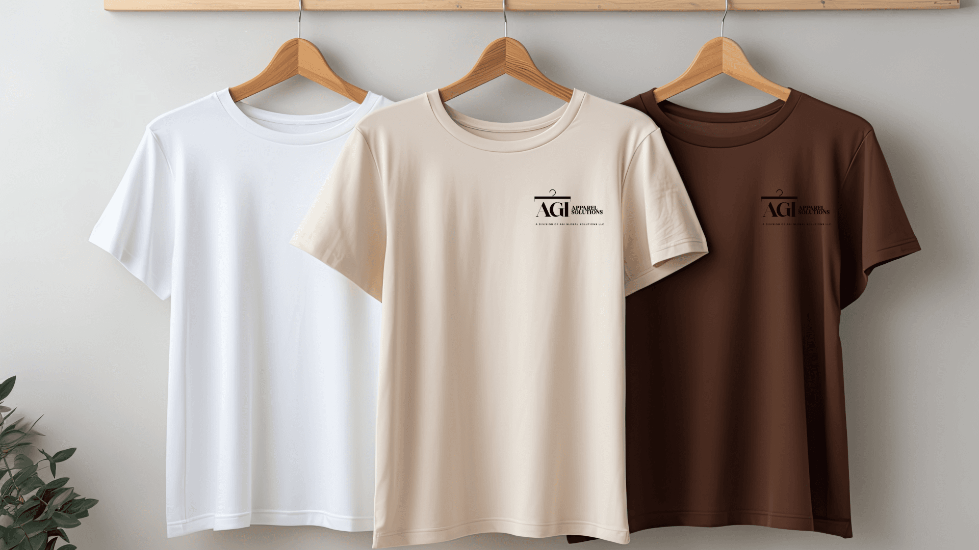 White, beige, and brown t-shirts with AGI Apparel Solutions logo hanging on wooden hangers.